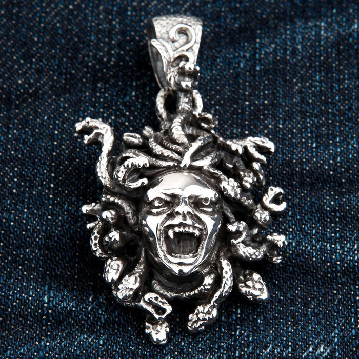 Close-up of the Medusa pendant's fangs and sharp snake scales resting on dark denim