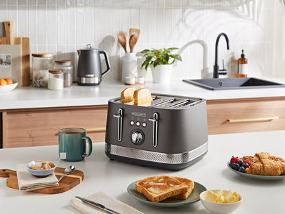 Gray toaster on a kitchen counter with toast, mugs, and fruit plate.