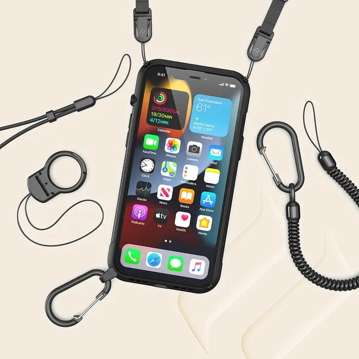 The Catalyst Case US iPhone 13 - Vibe Case (MagSafe compatible) in black is shown with a lanyard, carabiner clips, and detachable coiled wrist straps, arranged on a beige surface. The phone screen displays colorful app icons.