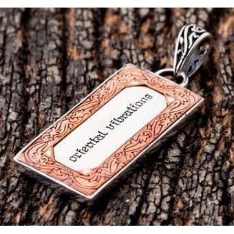 Copper border frames the engraved centre panel, with a scrollwork bail above, shot on tree bark.
