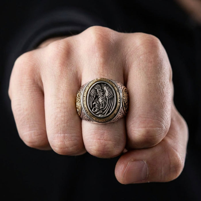 Close-up lifestyle shot of a man's clenched fist wearing a heavy silver and gold Japanese phoenix ring with intricate bird engravings against a dark background.