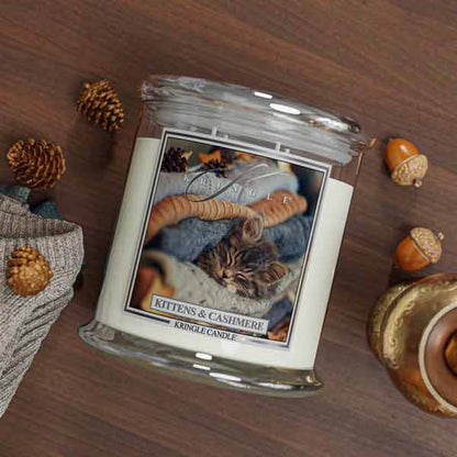 Kringle Candle jar with a kitten and cashmere 4-wick candle with cat label on a wooden surface with decorative elements.