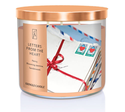 A three-wick candle in a clear glass jar with a bronze lid and a sentimental-themed label. The label features a bundle of vintage love letters tied with a red ribbon, with USA heart stamps on top. The candle’s wax is a soft peach shade, and the wicks are unlit. The scent notes listed are peony, blooming jasmine, and sandalwood.