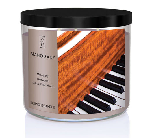 A three-wick candle in a clear glass jar with a black lid and a luxurious wood and music-themed label. The label features a polished mahogany piano with black and white keys, showcasing the deep reddish-brown wood grain. The candle’s wax is a rich brown, and the wicks are unlit. The scent notes listed are mahogany, driftwood, citrus, and fresh herbs.