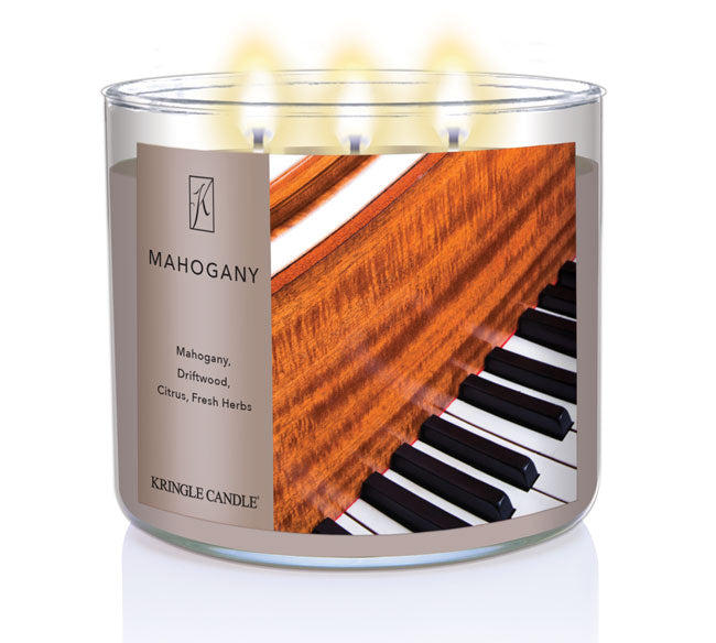 A three-wick lit candle in a clear glass jar with a luxurious wood and music-themed label. The candle’s wax is a rich brown, and all three wicks are burning.