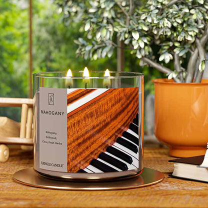 A three-wick lit candle in a clear glass jar with a luxurious wood and music-themed label. The candle’s wax is a rich brown, and all three wicks are burning.