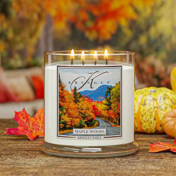 Kringle Candle with 'Maple Woods' labeled 4-wick on a wooden surface with autumn decorations.