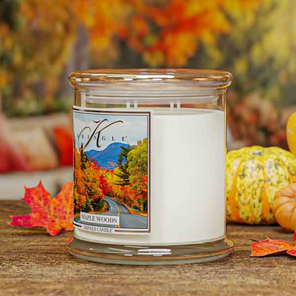 Maple Woods Scented 4-wick Candle with a scenic label on a wooden surface with autumn decorations