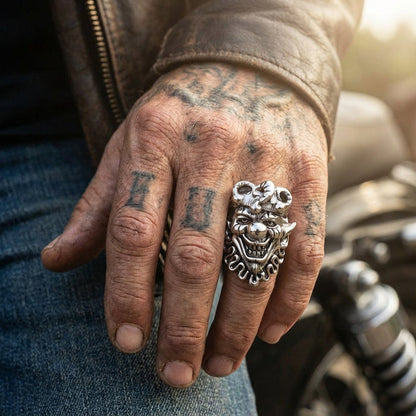 Silver joker skull ring with menacing face design worn on tattooed hand of biker wearing leather jacket showcasing edgy gothic style jewelry