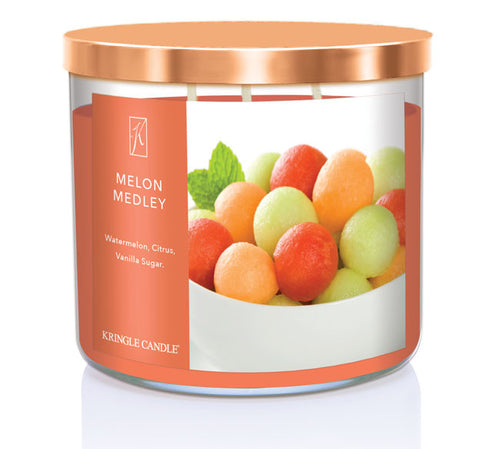 A three-wick candle in a clear glass jar with a bronze lid and a fresh fruit-themed label. The label features a bowl filled with colorful melon balls, including watermelon, cantaloupe, and honeydew. The candle’s wax is warm orange, and the wicks are unlit. The scent notes listed are watermelon, citrus, and vanilla sugar.