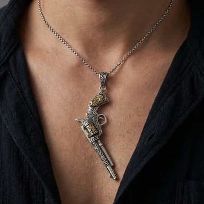Sterling silver Mexican gun pendant with gold accent details shaped like a vintage revolver, worn on a silver chain against a man's bare chest with dark open shirt
