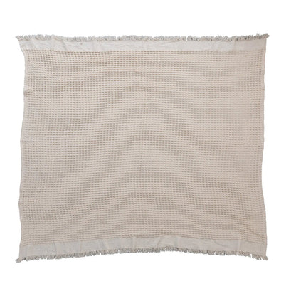 Beige cotton weave blanket featuring a waffle texture and fringe edges for a bohemian style