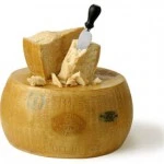 Parmigiano-Reggiano cheese wheel with slices and knife on top.