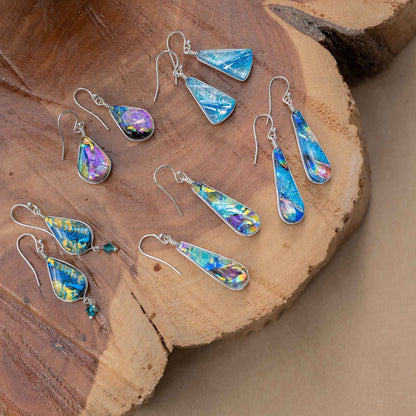 Five pairs of colorful dichroic glass earrings, featuring the Rainbow Falls, on a wooden platter.