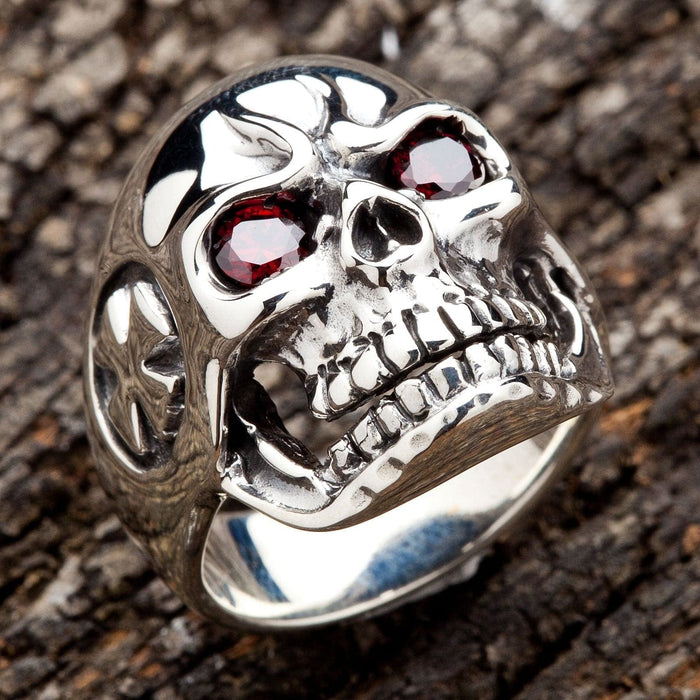 High-quality sterling silver skull ring with red eyes displayed on a wooden texture, showcasing detailed biker jewelry craftsmanship.