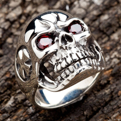 High-quality sterling silver skull ring with red eyes displayed on a wooden texture, showcasing detailed biker jewelry craftsmanship.