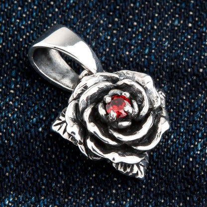 Close-up of the handcrafted silver rose pendant highlighting its intricate petal details, resting on a dark denim surface.