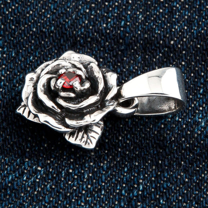 Sculpted petals and leaves wrap the red garnet centre, a tapered bail rising above, shot on denim.