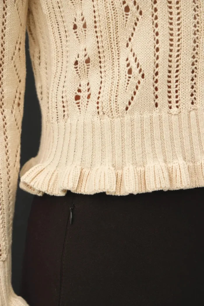 Cream-colored knitted ruffled pointelle crop cardigan with intricate lace patterns and ribbed ruffled hem design