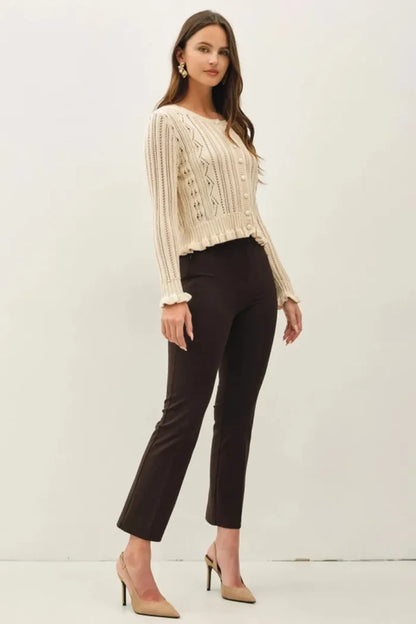 Cream-colored long-sleeved knit ruffled pointelle crop cardigan with intricate cable patterns and ruffled cuffs
