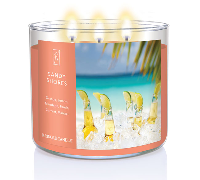 A three-wick lit candle in a clear glass jar with a tropical beach-themed label. The candle’s wax is soft coral, and all three wicks are burning.