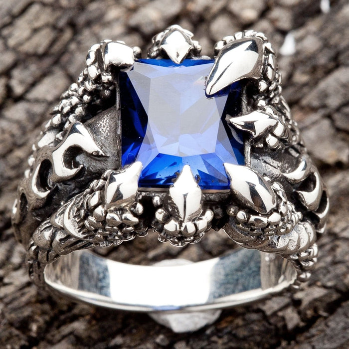 A gothic-style ring with monster talons holding a large blue sapphire, a piece of men's fantasy jewelry.