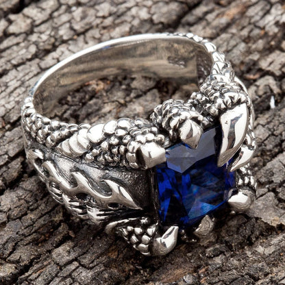 A heavy silver biker ring for men, designed with monstrous claws holding a large, square blue gemstone.
