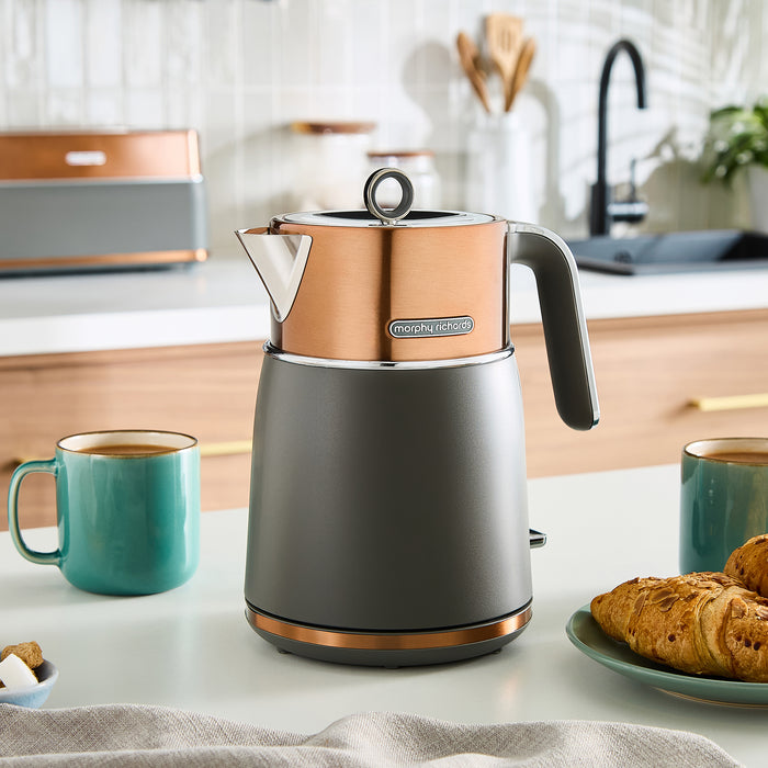 Grey and copper jug kettle on a kitchen counter with mugs and pastries.