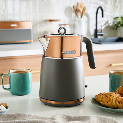 Grey and copper jug kettle on a kitchen counter with mugs and pastries.