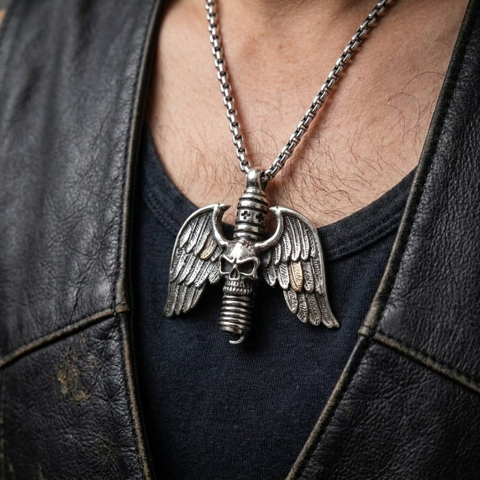 Close-up of a man wearing a silver gothic skull and wings pendant designed as a spark plug, hanging on a silver chain over a black t-shirt and distressed black leather vest.
