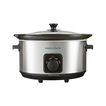 A Morphy Richards stainless steel 6.5L slow cooker with a black glass lid and brushed stainless steel body, featuring a control knob on the front.