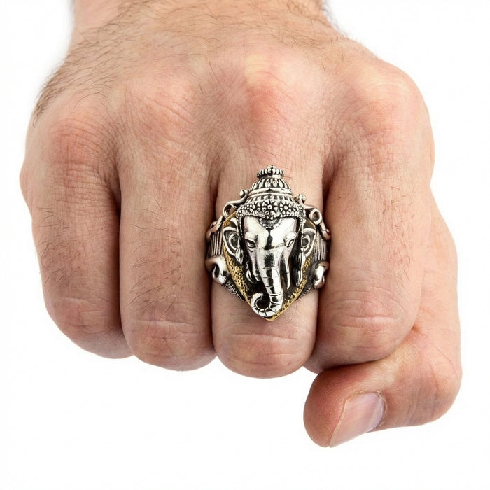 Silver Ganesh Hindu God ring with detailed elephant head design and ornate crown worn on a man's middle finger, showcasing intricate craftsmanship with gold-toned accents on a clenched fist against a white background