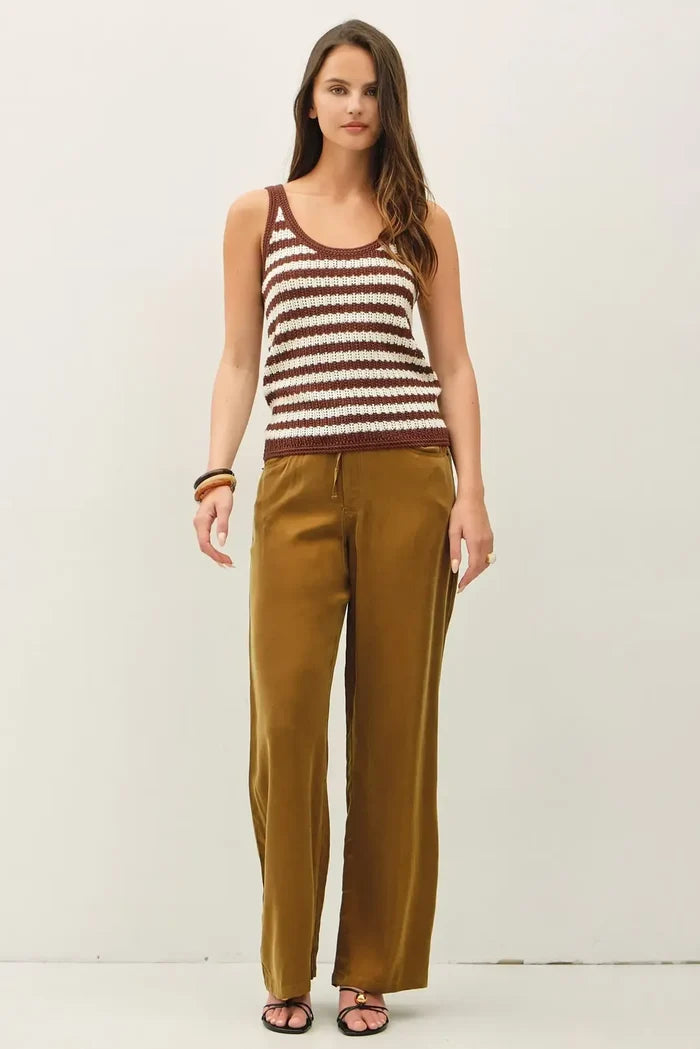 A woman wears a textured stripe tank sweater in brown and cream knitted fabric paired with olive green satin trousers
