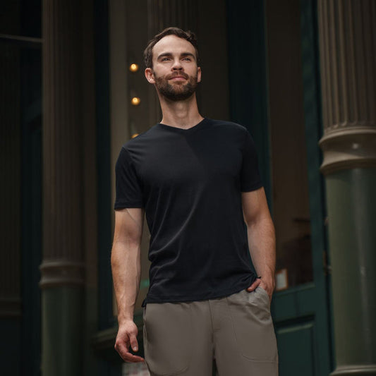 Man wearing a black t-shirt and beige pants standing in front of a dark building entrance.