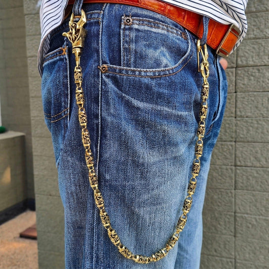 Solid brass wallet chain worn on blue jeans, clipped belt loop to front pocket beside a tan crocodile belt.