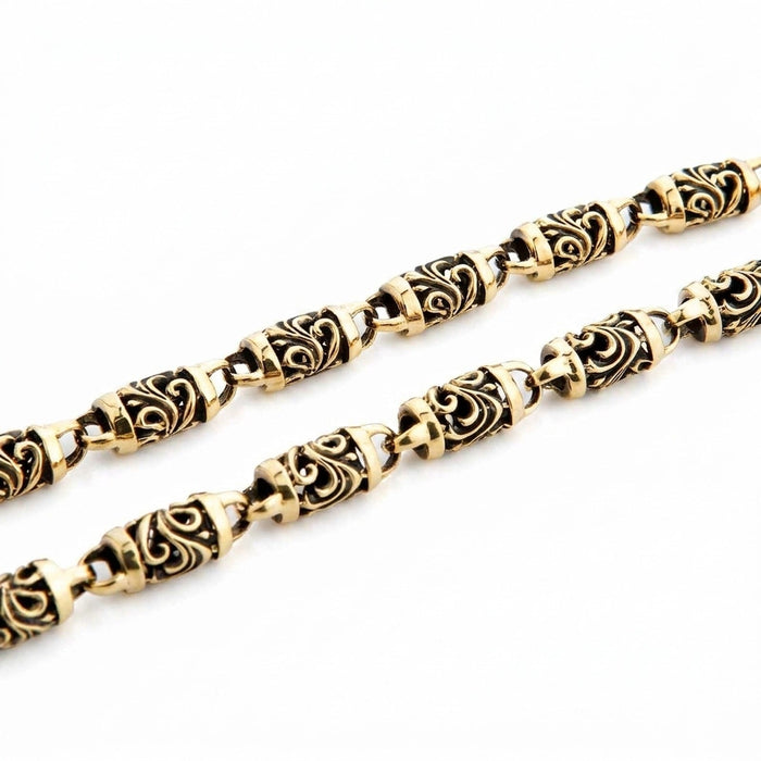 Macro view of the 8mm carved barrel links, tribal scrollwork darkened in the recesses against polished brass.
