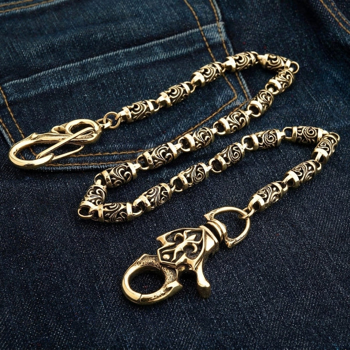 Angled shot of the polished brass chain on dark denim with the carved scroll face of the lobster claw turned up.
