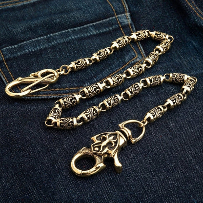 Angled shot of the polished brass chain on dark denim with the carved scroll face of the lobster claw turned up.