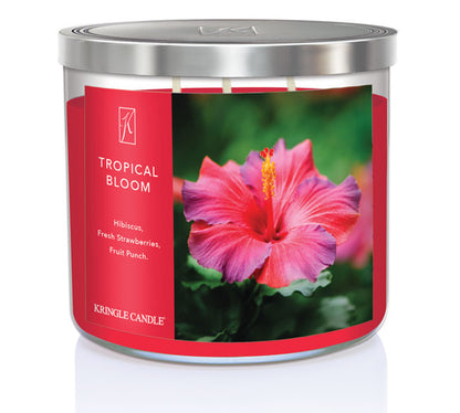 A three-wick candle in a clear glass jar with a gold lid and a vibrant floral-themed label. The label features a lush tropical arrangement of hibiscus flowers, bright pink and red petals, and green leaves. The candle’s wax is hot pink, and the wicks are unlit. The scent notes listed are hibiscus, strawberries, and fruit punch.