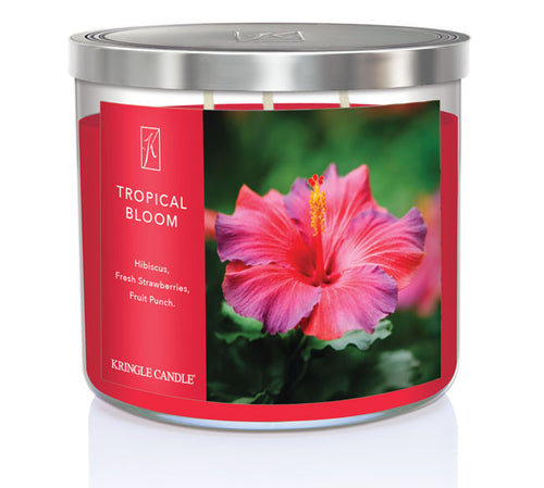 A three-wick candle in a clear glass jar with a gold lid and a vibrant floral-themed label. The label features a lush tropical arrangement of hibiscus flowers, bright pink and red petals, and green leaves. The candle’s wax is hot pink, and the wicks are unlit. The scent notes listed are hibiscus, strawberries, and fruit punch.