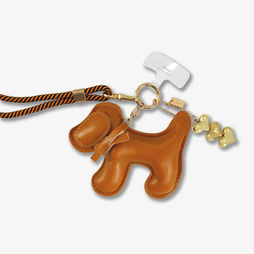 Detail of crossbody phone strap with brown plush dog charm, gold hardware and black and orange cord on white background