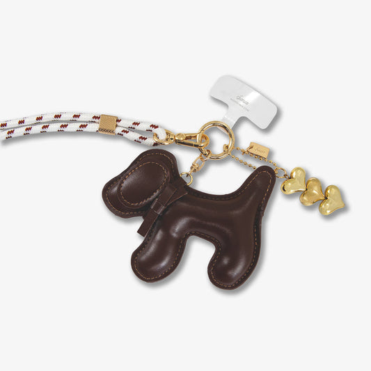 Close-up of Universal crossbody phone strap showing chocolate plush dog charm, braided white-and-brown rope strap and gold hardware on white background