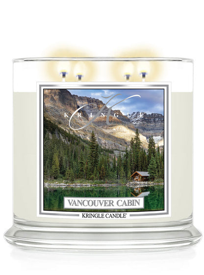 Four-wick candle lit, featuring a scenic label of a lakeside cabin surrounded by trees and mountains,  "Vancouver Cabin"