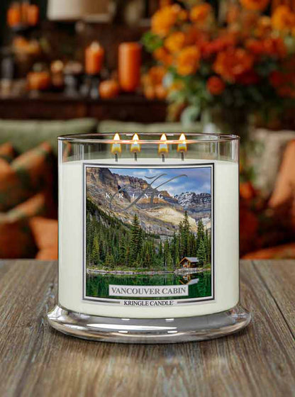 Four-wick candle lit, featuring a scenic label of a lakeside cabin surrounded by trees and mountains,  "Vancouver Cabin"