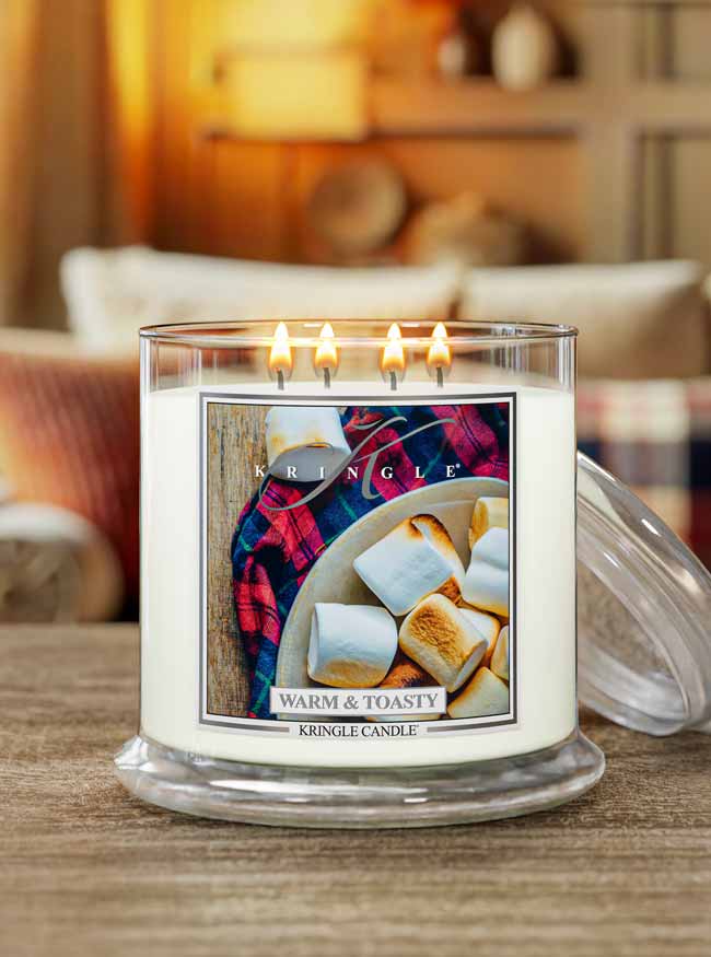 Kringle Candle with Warm and Toasty scented 4-wick lit candle with marshmallows and plaid fabric on a wooden surface