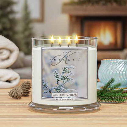 Kringle Candle in Winter Cypress scent on a wooden surface with a fireplace in the background